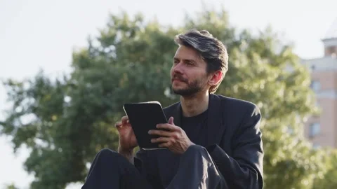 Young guy browsing tablet in garden. Thoughtful businessman decide to invest Stock Footage 251562756
