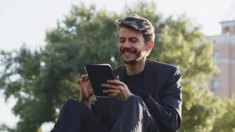 Young guy browsing tablet in park. Satisfied adult man using tablet sending Stock Footage 252608534