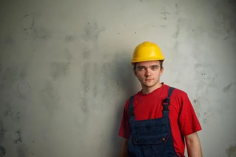 Young guy builder in a red T-shirt, blue robe and yellow construction helmet Stock Photos