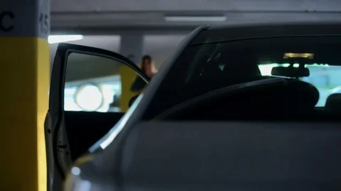 Young guy on car meets soy girl in covered parking lot. rear view. young couple  Stock Footage 129393836