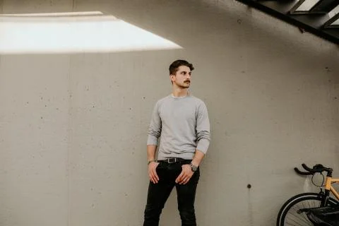 The young guy in casual clothes posing with bicycle over grey wall. Outdoor. Stockfoto's