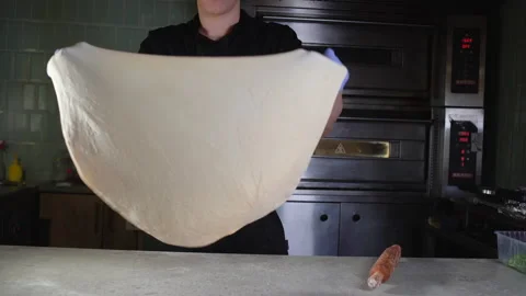 Young guy in chef uniform twirls and throws pizza dough in the restaurant Stock Footage 148465386