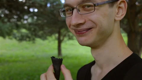 A young guy chews a black ice cream cone and shows someone a vanity shot. Side v Stock Footage 102156016