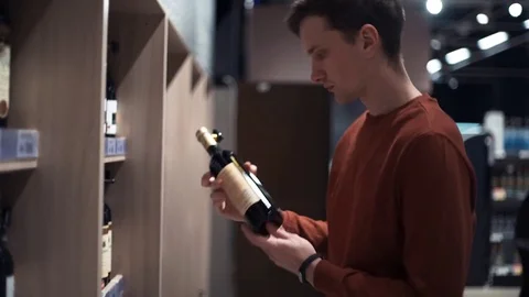 Young guy chooses wine looking at bottles at supermarket Stock Footage 82990813