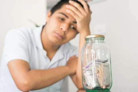 Young guy crestfallen looking at his savings in a glass jar. young man next t Stock-Fotos