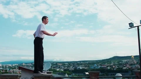 A young guy dances hip-hop while standing on a parapet against the blue sky. Imp Stock Footage 242146243