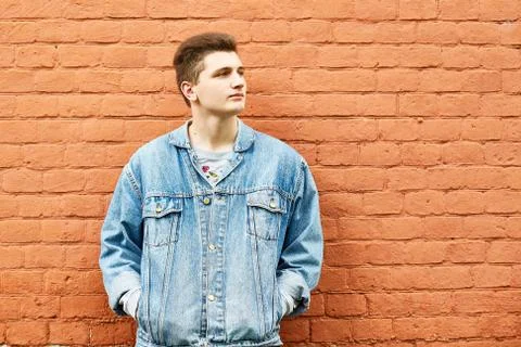 Young guy in a denim jacket against a brick wall. copyspace Stock Photos