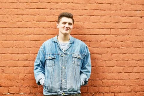 Young guy in a denim jacket against a brick wall Stock Photos
