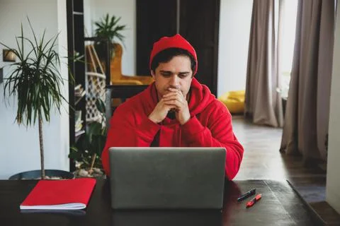 Young guy developer in red clothes working with computer at home office Stock Photos