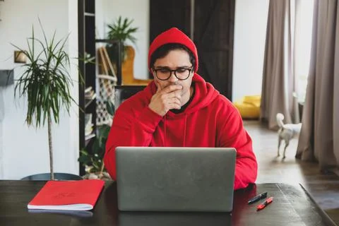 Young guy developer in red clothes working with computer at home office Stock Photos