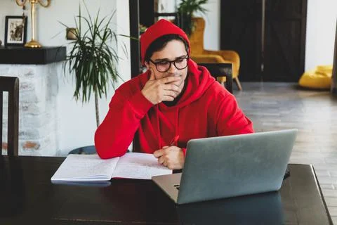 Young guy developer in red clothes working with computer at home office Stock Photos