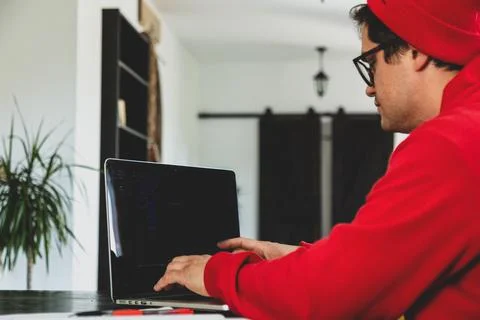 Young guy developer in red clothes working with computer at home office Stock Photos