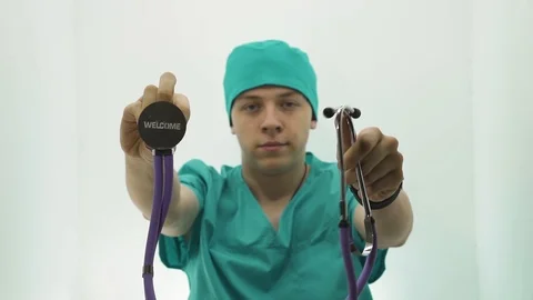 Young guy in a doctor's costume shows a phonendoscope with a sign welcome Stock Footage 107009028