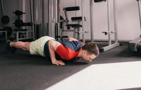 A young guy does push-ups from the floor in the gym during a workout. healthy Stock Photos
