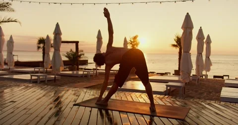 A young guy does yoga and takes different positions of his body at the dawn of Stock Footage 249310648