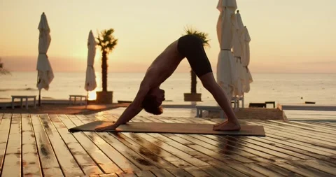 A young guy does yoga on a sunny beach covered with planks in the morning Stock-Footage 249435640