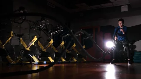 Young guy doing an exercise with rope in gym with contour light. Slow motion Stock Footage 168969378