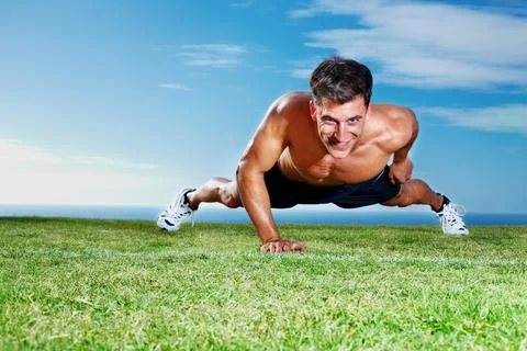 Young guy doing single handed pushups on the field. Portrait of a young guy Stock Photos