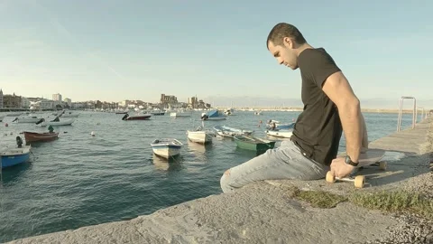 Young guy dressed in blue jeans and black short sleeve t-shirt sitting on pie Stock Footage 141539564