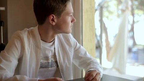 Young guy dressed in white upset looking out the window Stock Footage 113598835