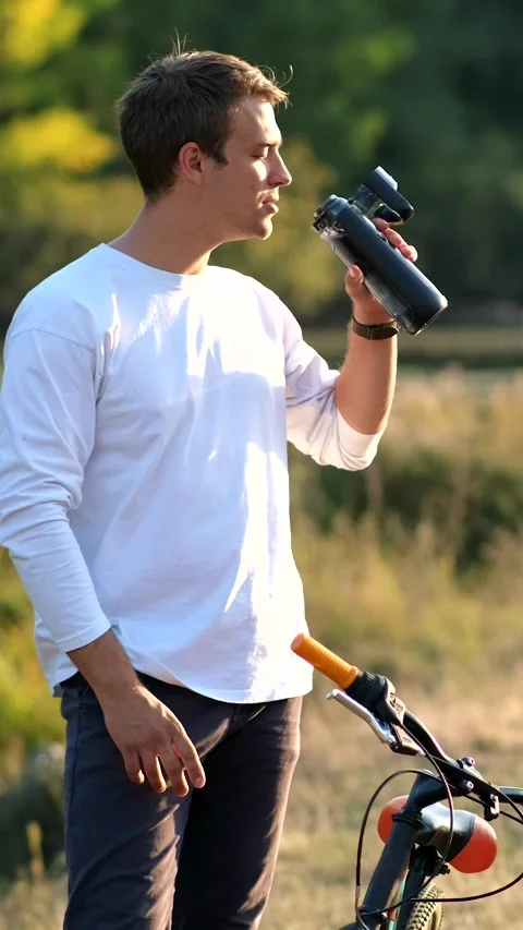 Young guy drinking clean water next to his bike on the river bank. The conc.. Video stock 305847431