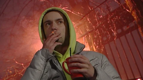 A young guy drinking hot tea or coffee from a red mug, Smoking a cigarette Stock Footage 120577830