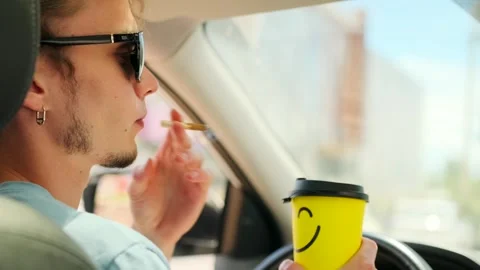 A young guy drinks coffee while sitting in a car relaxingly smoking a cigarette Video stock 279396527