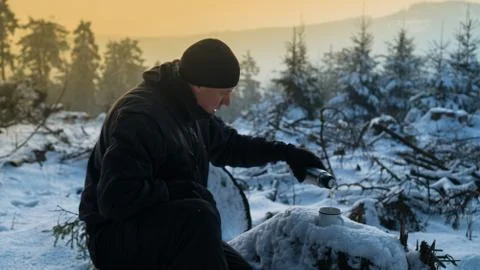 Young guy drinks hot tea from a thermos in the winter morning in the mountains Stock Photos