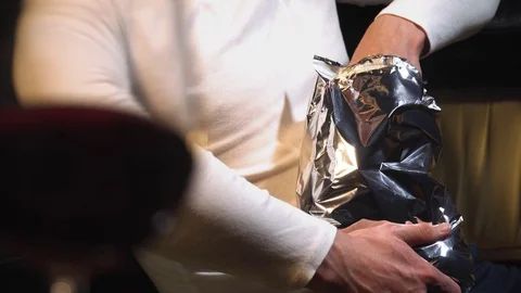 Young guy eats food with full hands from the packaging, being at home Stockbeeldmateriaal 129146002