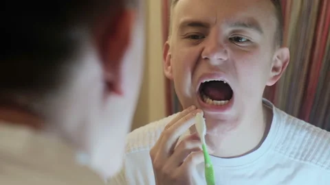 Young guy examines his teeth in the mirror Stock Footage 122735742