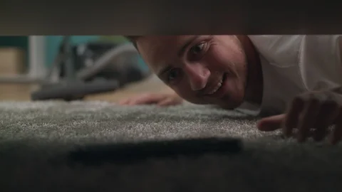 A young guy finds a lost tv remote under the sofa in the living room 스톡 동영상 108026391