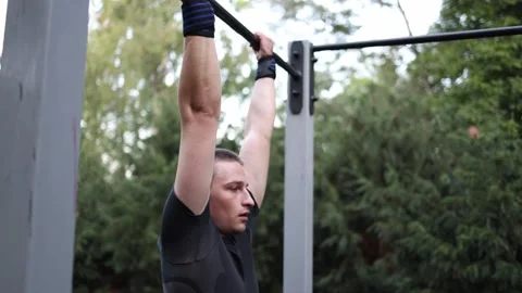 Young guy focuses on pull ups gripping the bar with strength in outdoor workout  Stock Footage 316701718
