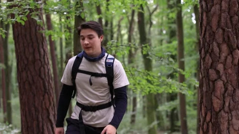 Young guy in forest looks around and goes for a walk in sportswear and backpack Vidéo 252514687