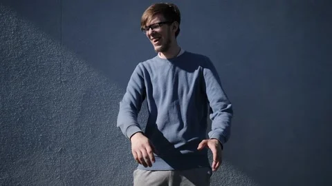 Young guy with glasses dancing in a blue shirt against a blue wall Stock Footage 130508414
