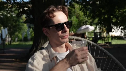 A young guy with glasses drinking a cold drink on a summer terrace. close-up Stock Footage 279745562