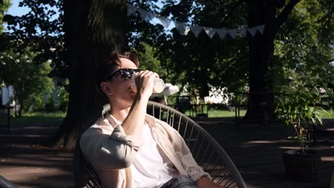 A young guy with glasses drinking a cold drink on a summer terrace. close-up Stock Footage 279745563