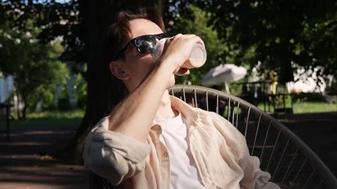 A young guy with glasses drinking iced coffee on a summer terrace Stock Footage 280325768