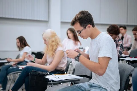A young guy with glasses during a physics test takes pictures of a test on his Stock Photos