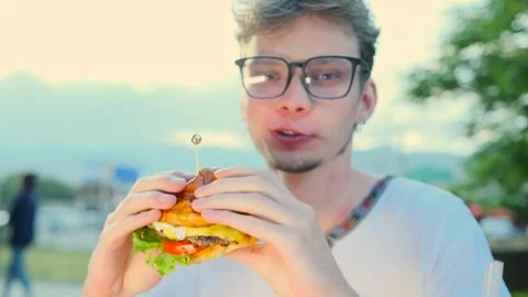 A young guy in glasses eats an appetizing burger with meat Stock Footage 279396643