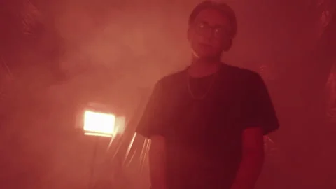 A young guy with glasses sits in a dark room, the room is in smoke, looks at the Stock Footage 132416143