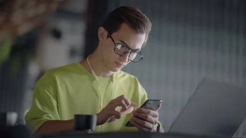 Young guy with glasses is sitting at table in cafe with laptop and typing Stock Footage 344800224