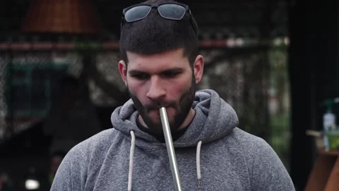 Young guy in glasses smokes hookah, exhales smoke into camera cottage Vidéo 137583900