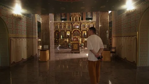 Young guy goes inside the orthodox church and examines the rich interior with 库存影片 236565639