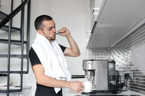 A young guy is going to work in the morning. Brushes teeth near a coffee mach Stock Photos
