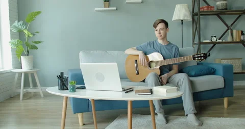 A young guy in a good mood communicates on the Internet plays guitar and sings a Vídeos de archivo 130467893