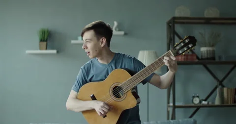 A young guy in a good mood plays the guitar and sings a song at home Stock Footage 130460895