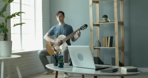 A young guy in a good mood plays the guitar at home Vídeos de archivo 130670911