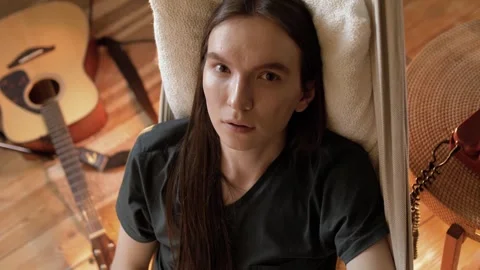 Young guy with a handsome face and long hair lies in a hammock in an apartment Stock Footage 245992184