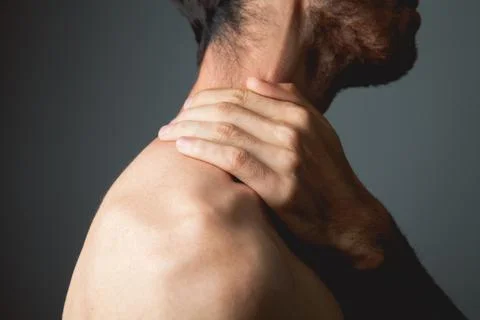 A young guy has a shoulder ache on a gray background Stock Photos