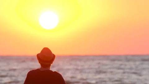Young guy in a hat watching the sunset by the ocean, sea Stock Footage 137972442